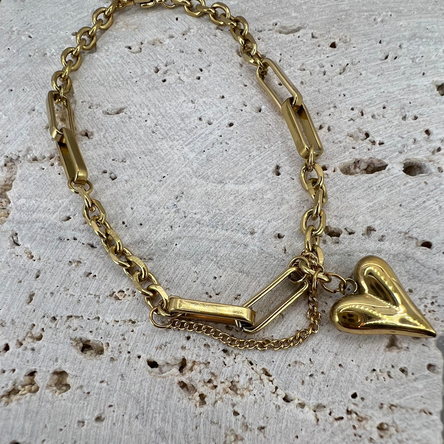 Gold chain bracelet with a heart-shaped charm on a textured surface