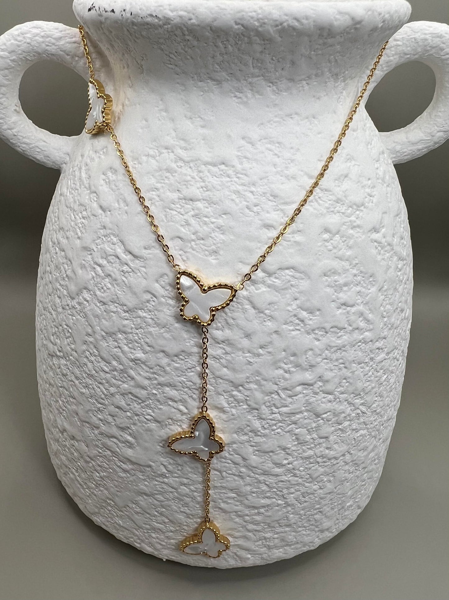 Gold necklace with butterfly pendants on a textured white vase