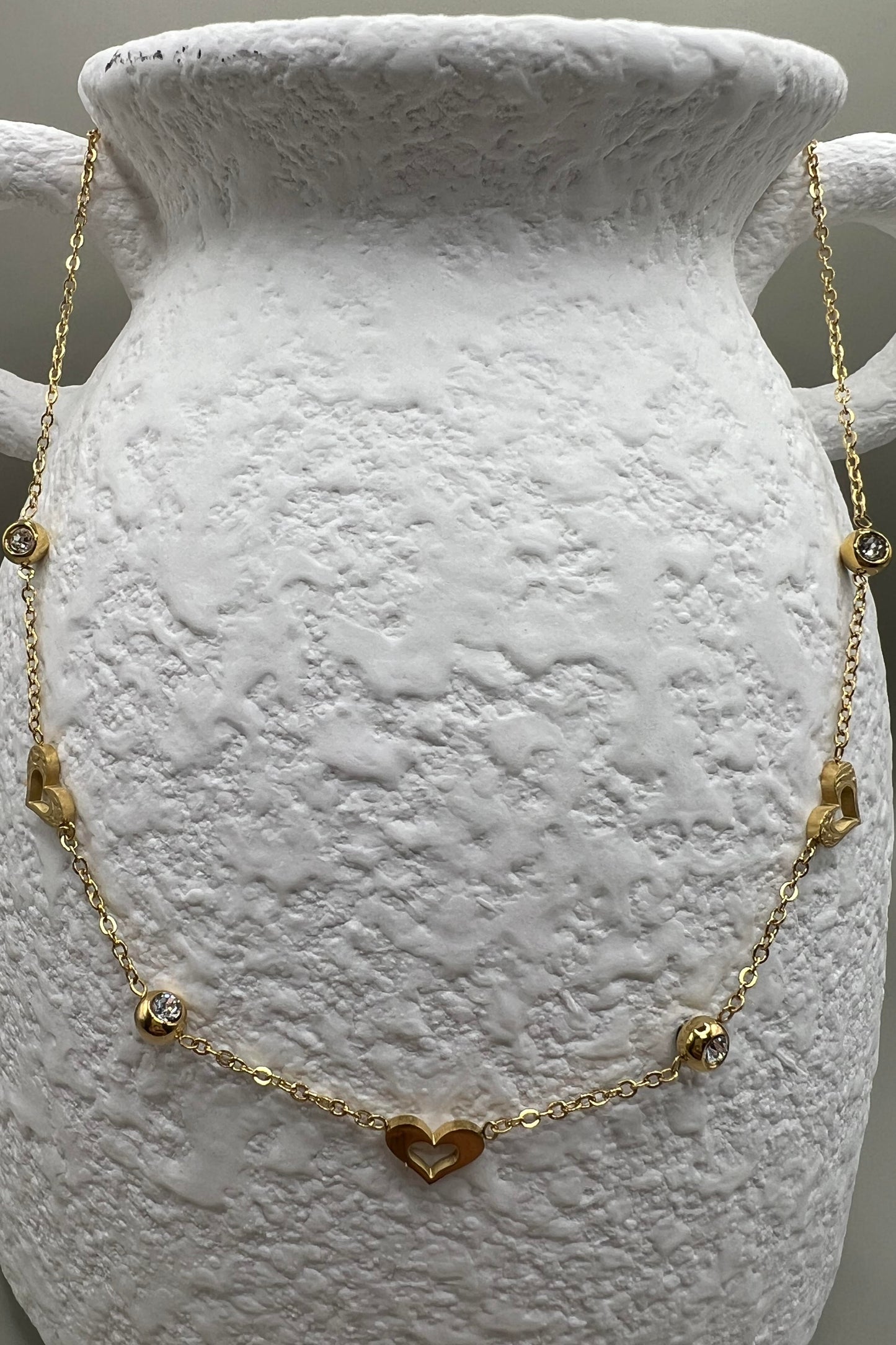 A gold-colored necklace with heart-shaped pendants and small dangling charms displayed on a white textured surface.