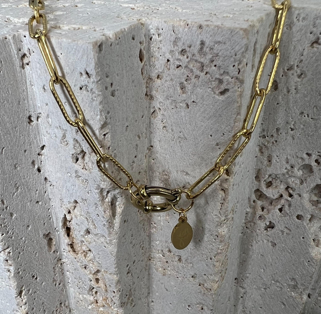 Gold chain necklace with a pendant on a textured stone surface