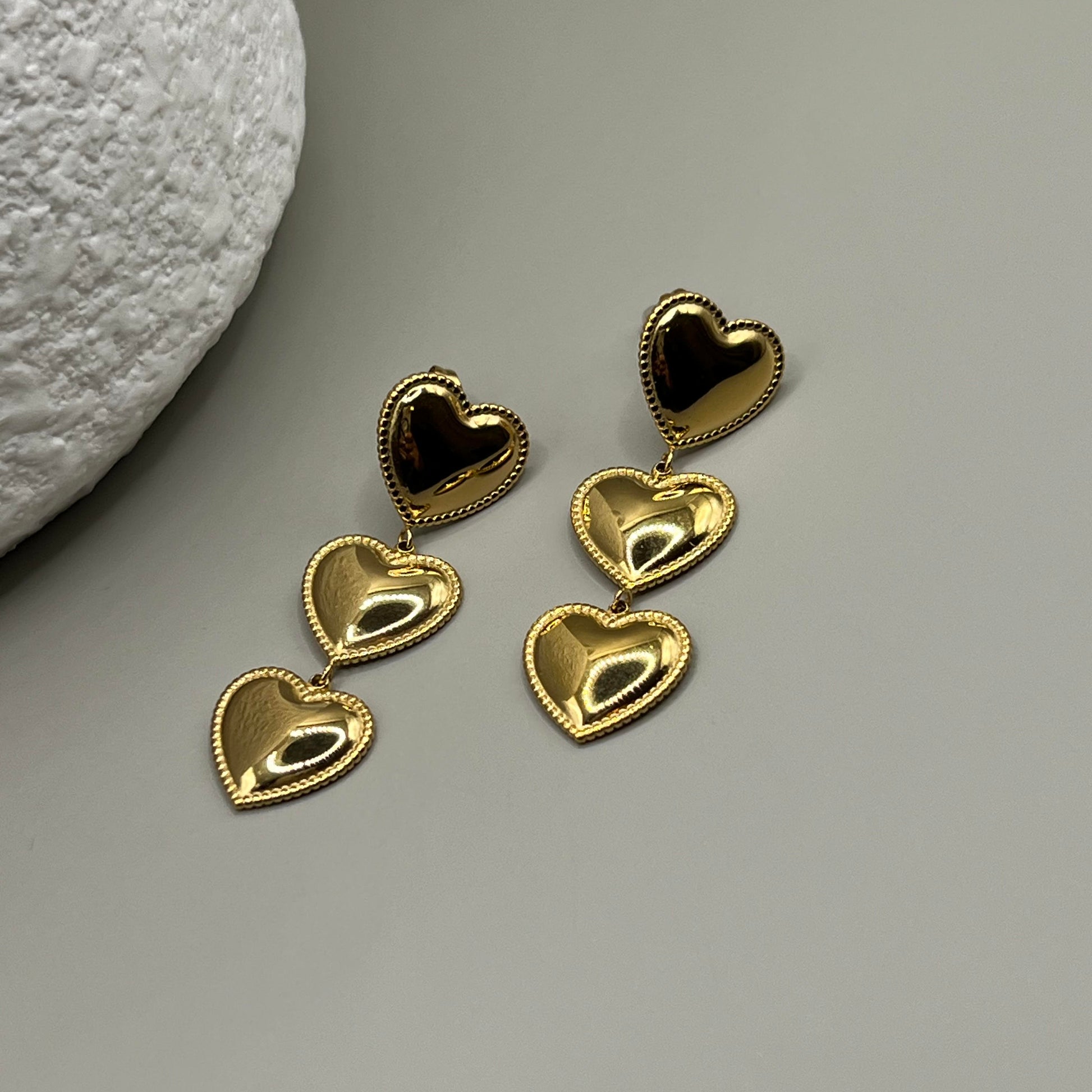 Gold heart-shaped earrings on a gray surface with a textured white object.