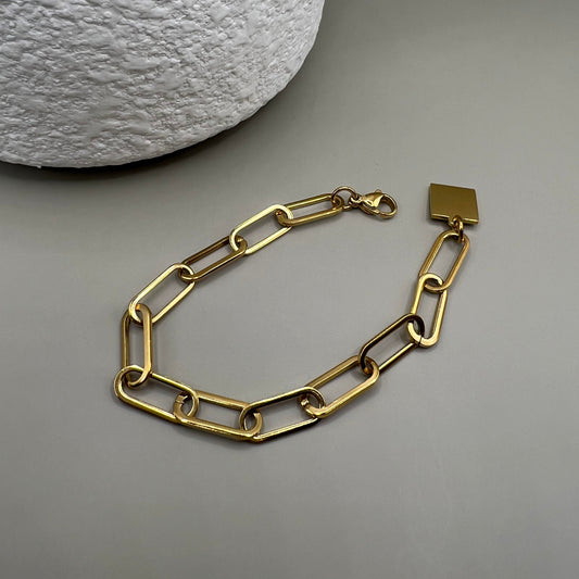 A gold-colored bracelet featuring a chain structure and a square-shaped paperclip detail.