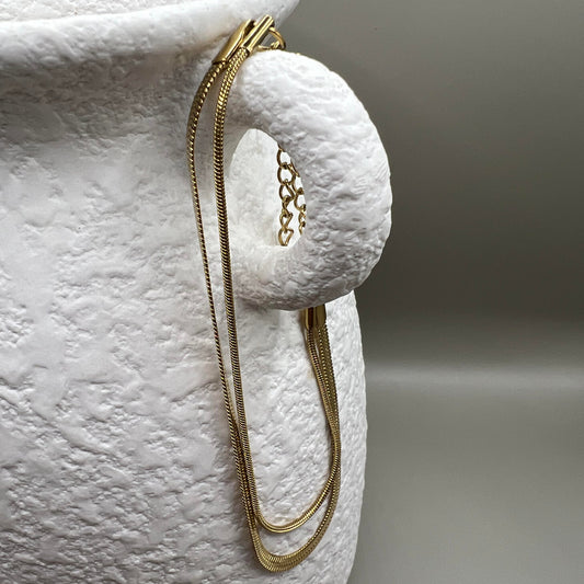 A gold-colored bracelet with a chain link strap, displayed on a textured white surface.