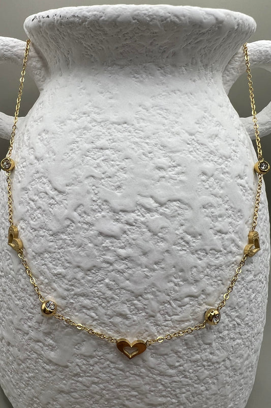 A gold-colored necklace with heart-shaped pendants and small dangling charms displayed on a white textured surface.